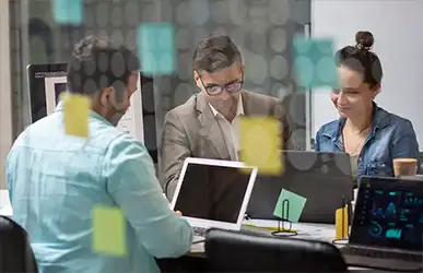 Three professionals collaborating at a modern office with laptops and analytics dashboard