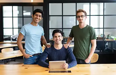 Three young professionals in a modern office, smiling and posing with a tablet