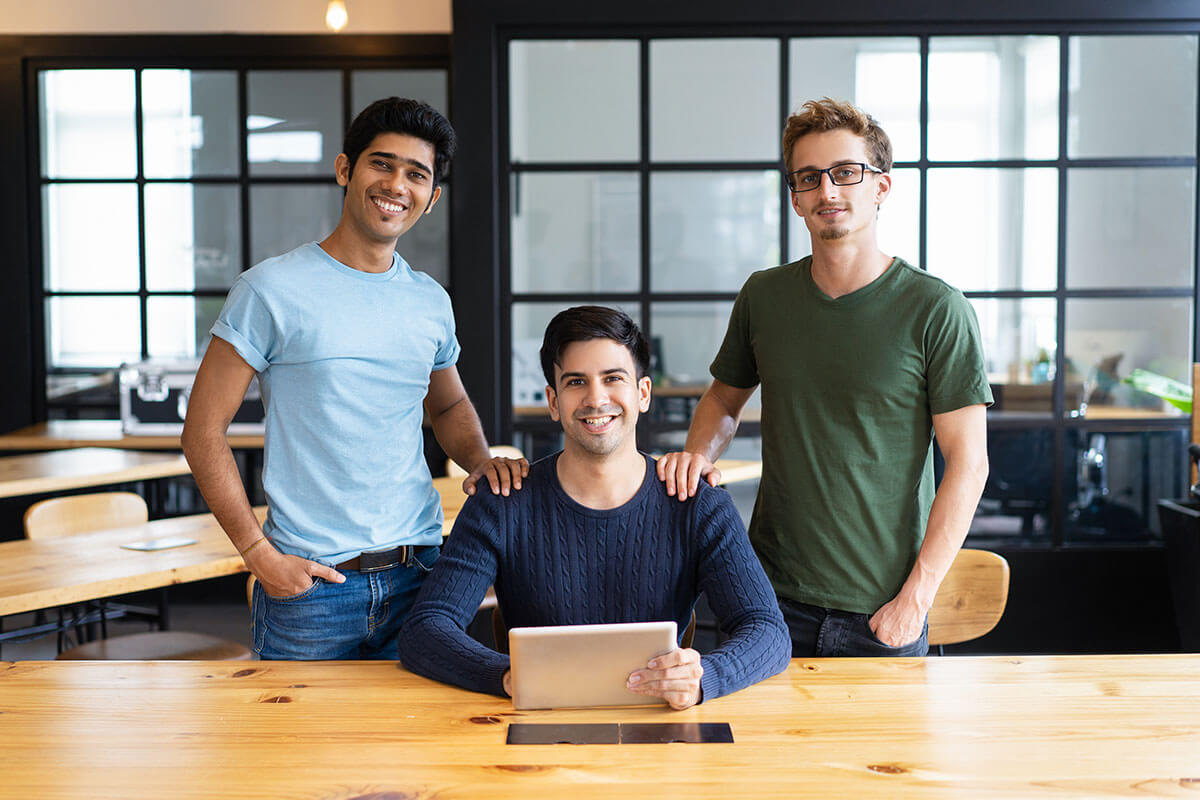 Tres jóvenes profesionales en una oficina moderna, sonriendo y posando con una tablet